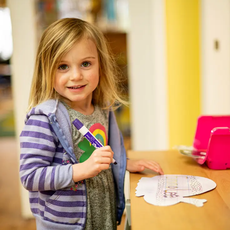 LIttle School student smiling at camera while holding a marker