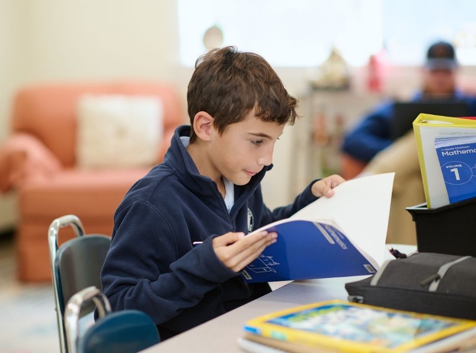 Kent School student sitting down and opening a notebook during classroom instruction